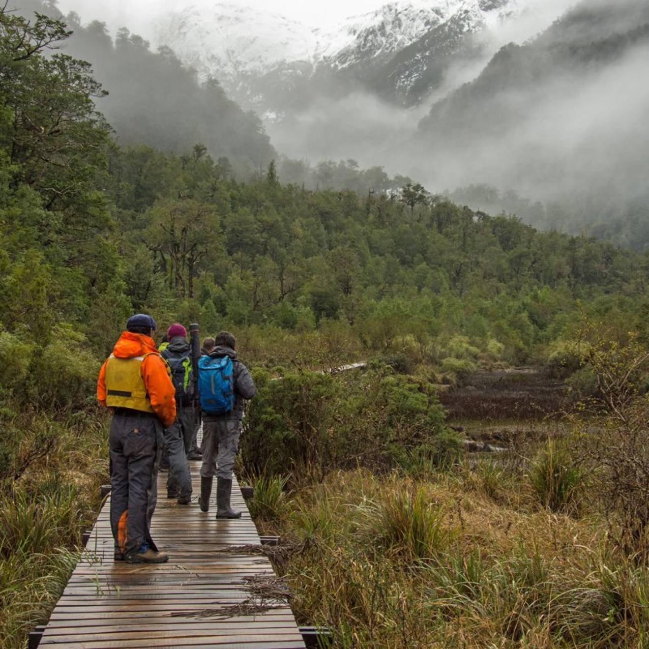 People on a boardwalk in Patagonia looking into foggy valley