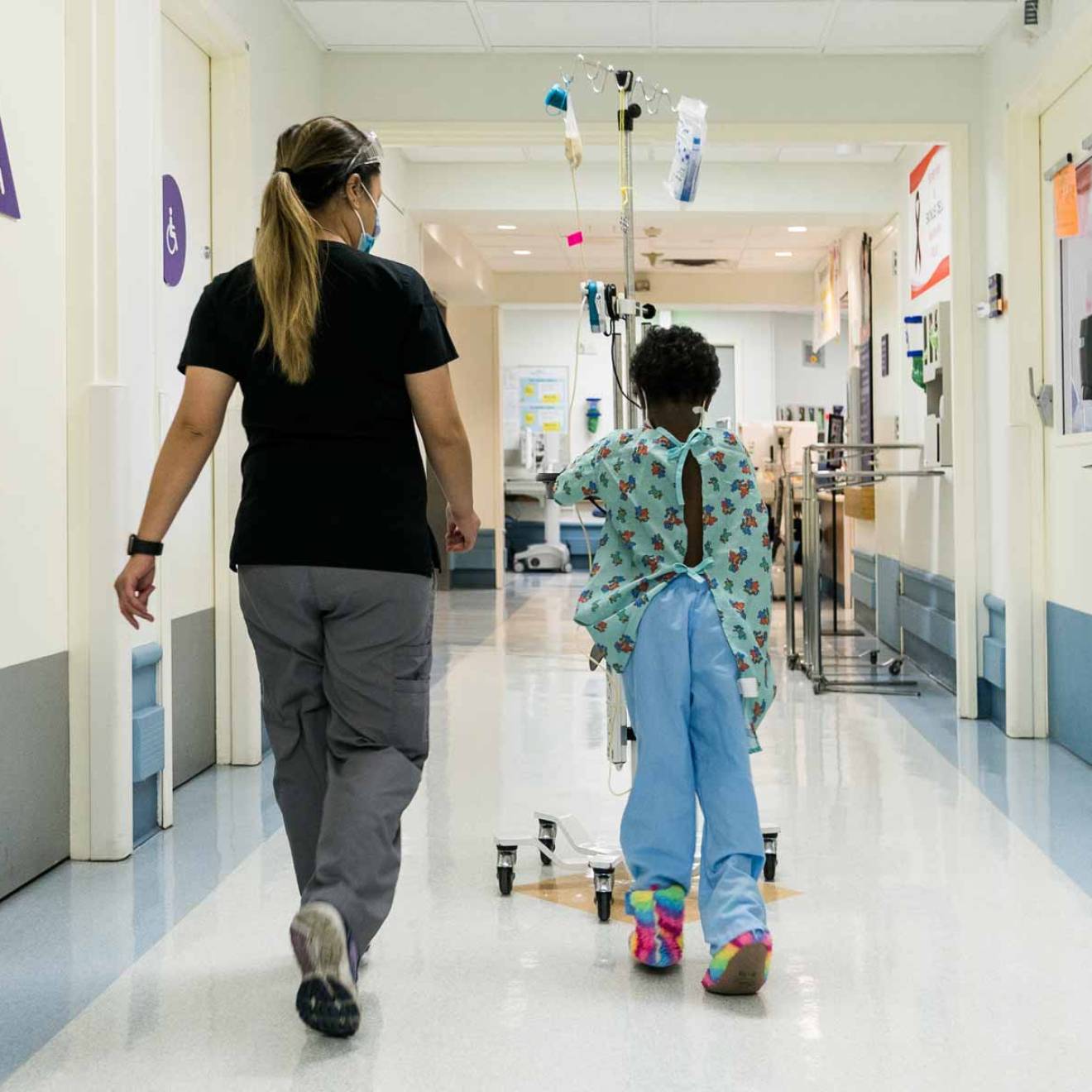 a nurse wearing a mask walks with a young Black patient around a hospital unit