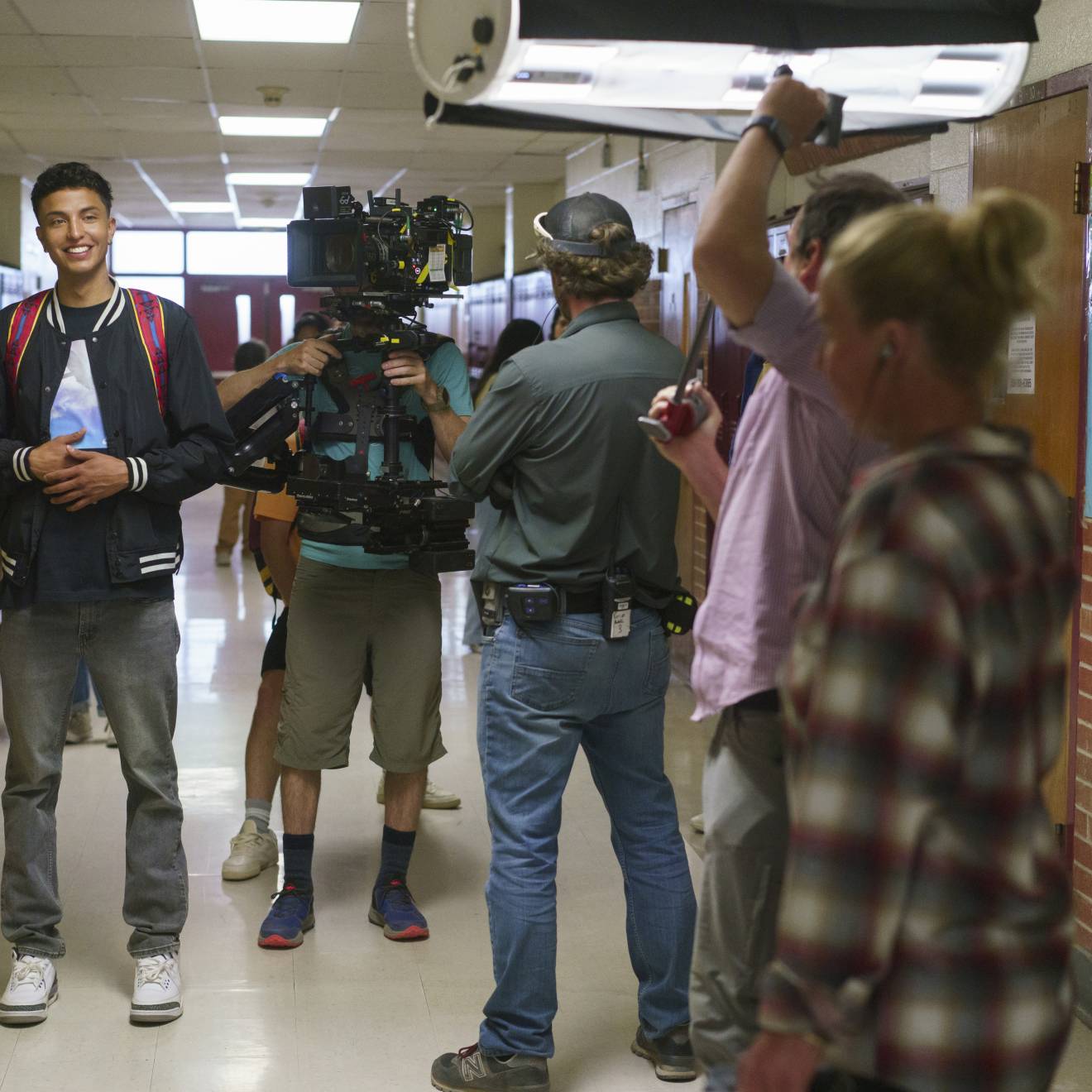 A young man smiling in a busy high school hallway being filmed as part of the movie Rez Ball