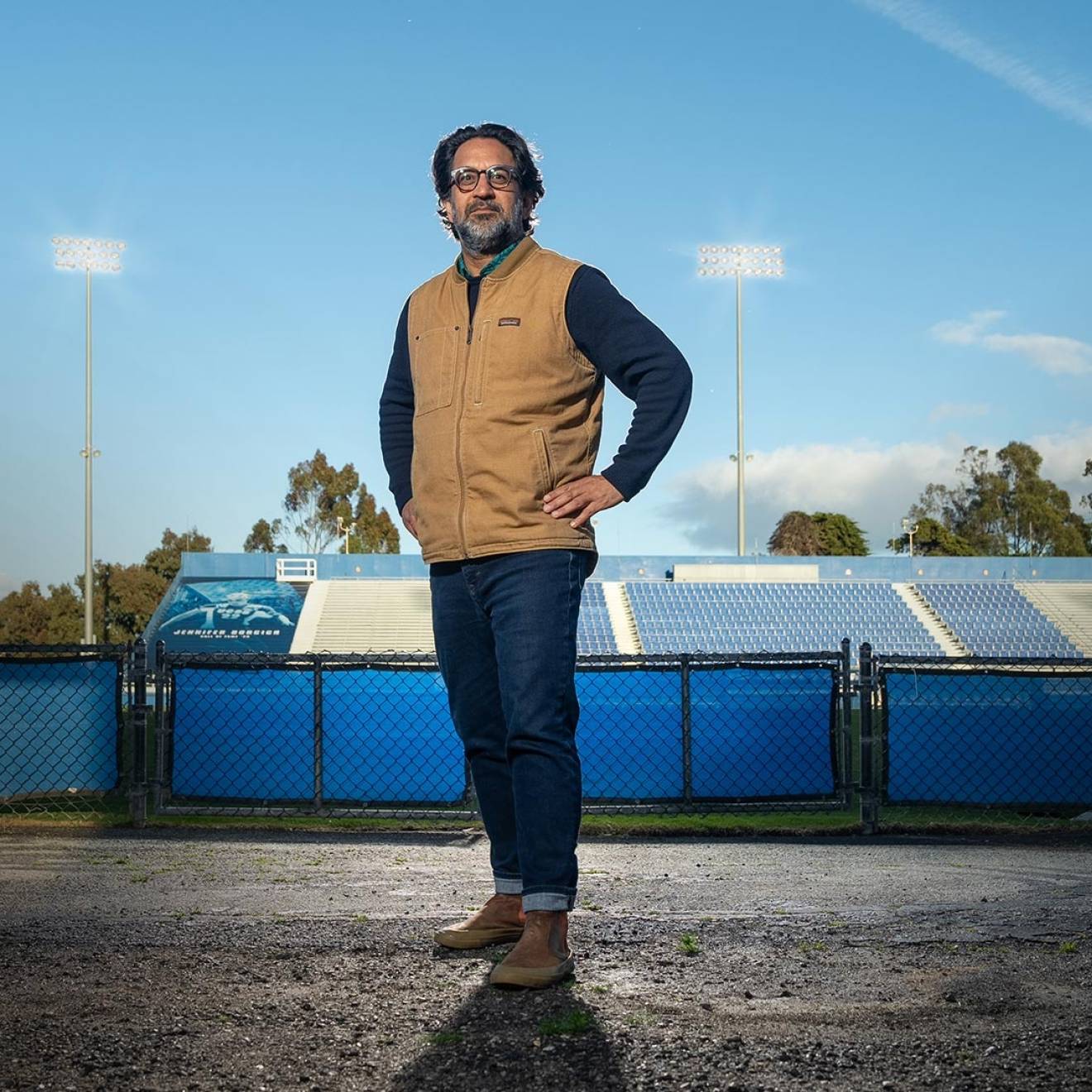 Man with salt and pepper beard stands at ground-level field entrance of a stadium, field behind him