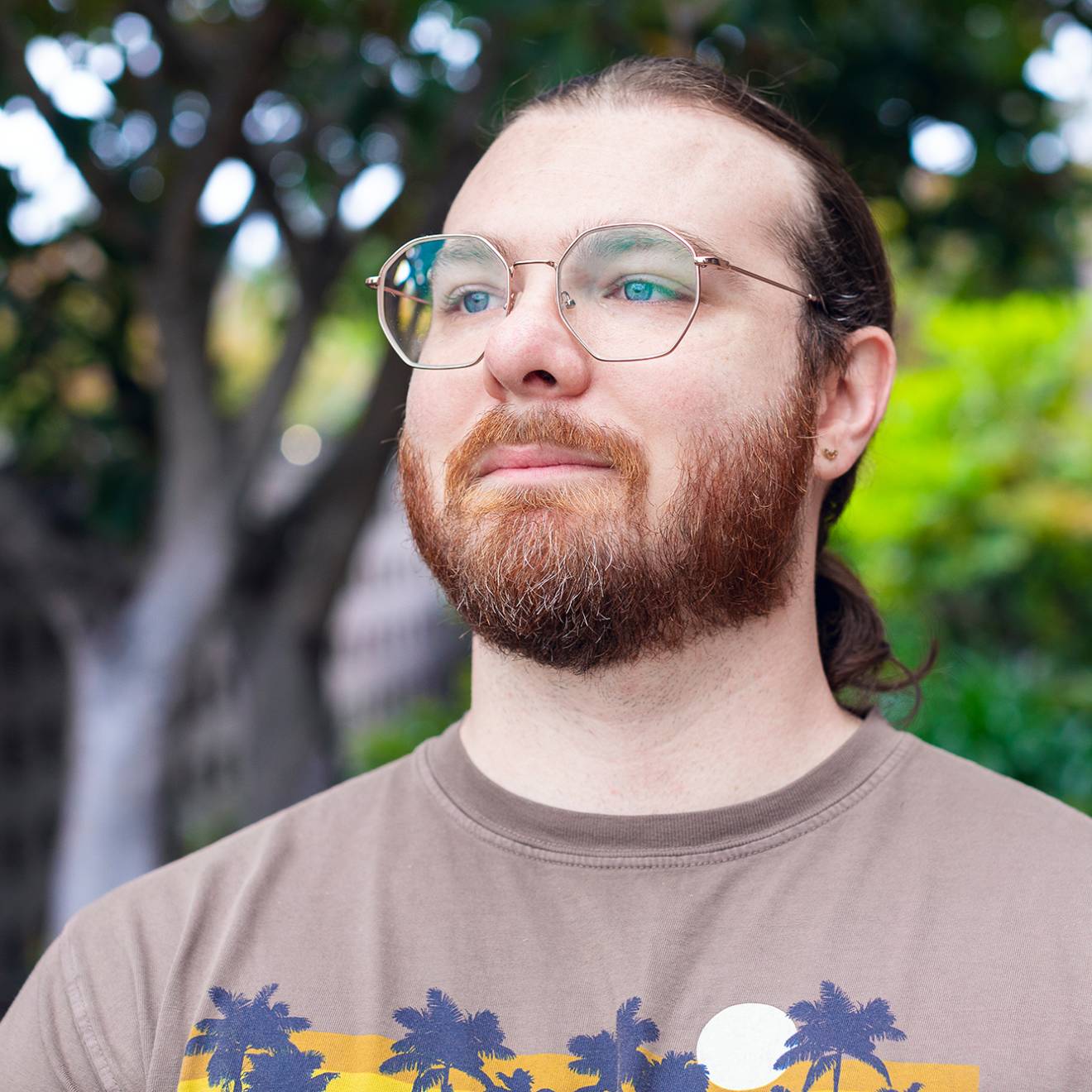 A man with a beard and pony tail wearing a T-shirt and glasses gazing into the distance