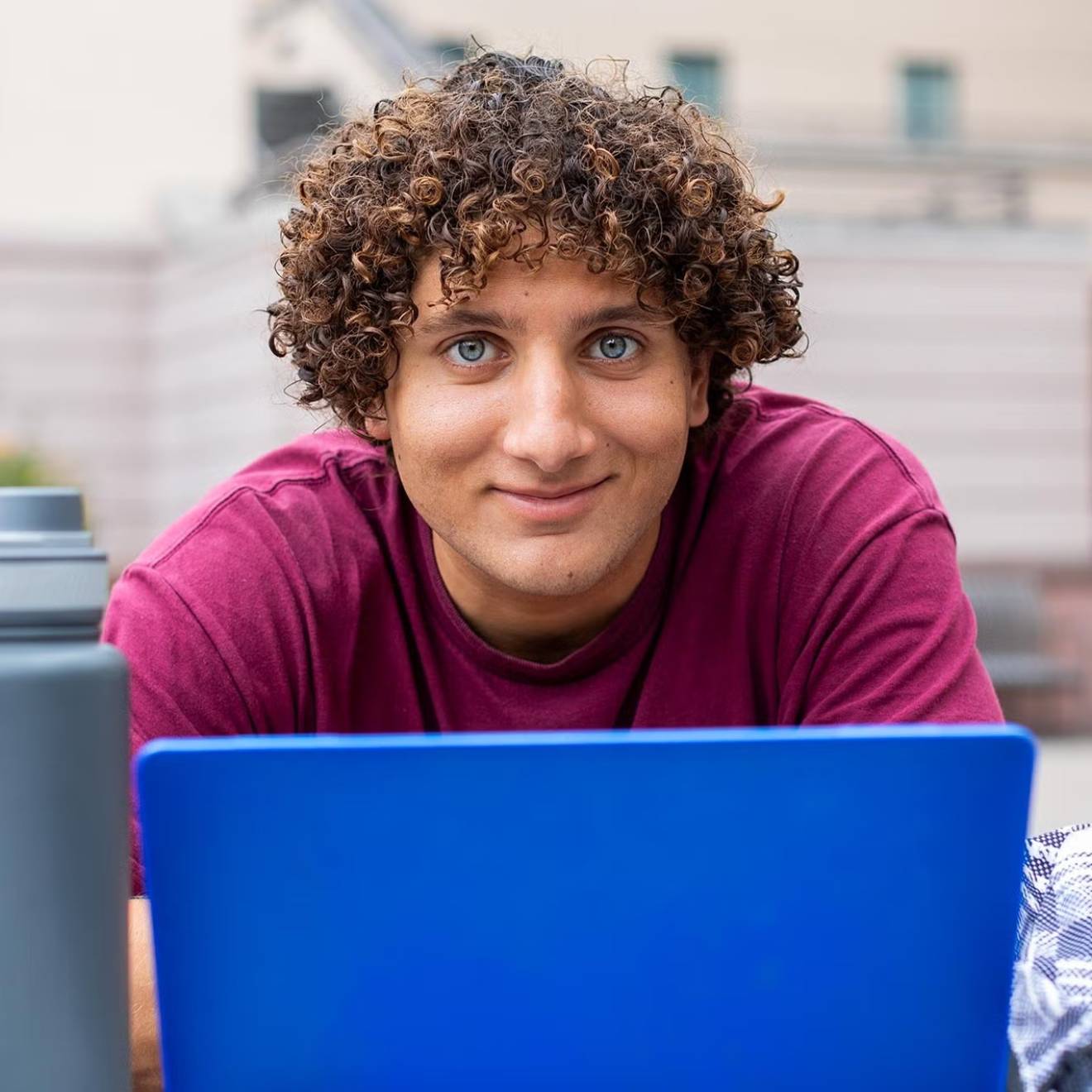 Learning curiosity A young man with curly hair stares intently above a laptop while sitting outdoors