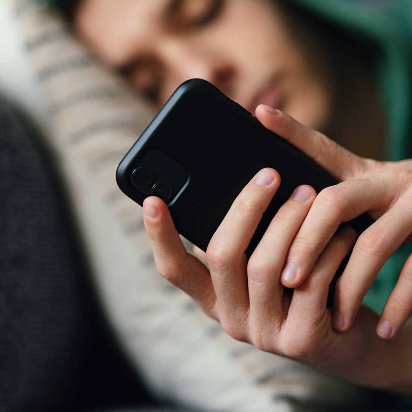 A teen, slightly out of focus, lying on the couch, looking at phone