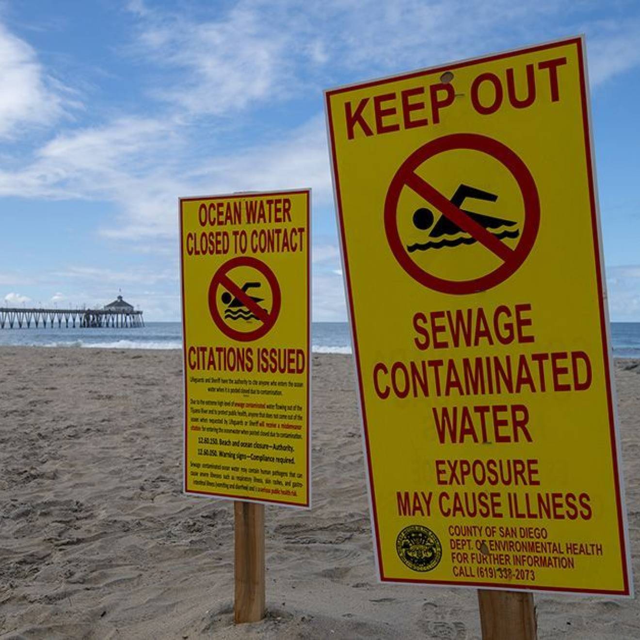 Closed beach An empty beach with a pier in the background on a nice day bears signs that say Keep Out Sewage Contaminated Water and Ocean Water Closed to Contact Citations Issued