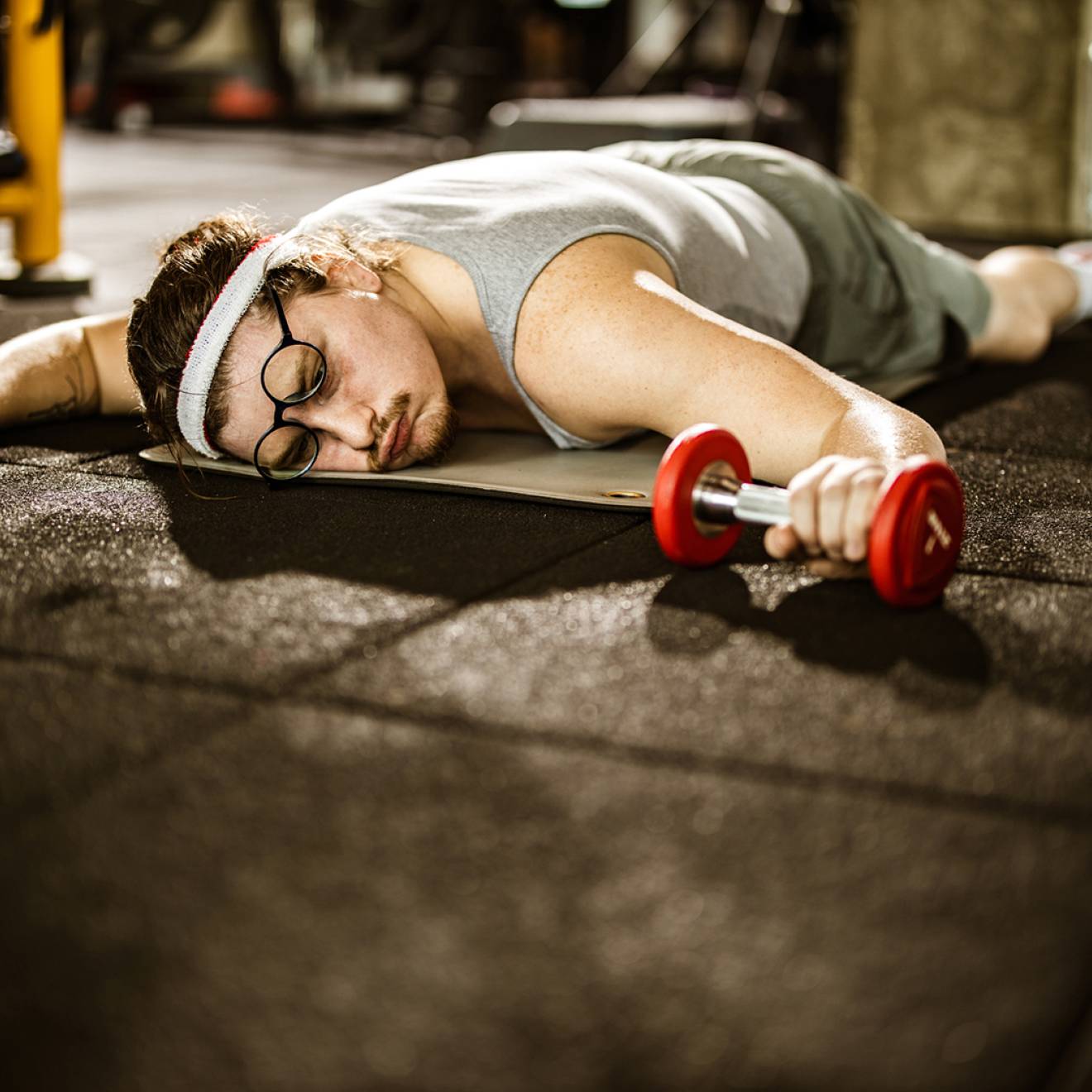 Male athlete lying on the floor, feeling exhausted after sports training with dumbbells in a gym