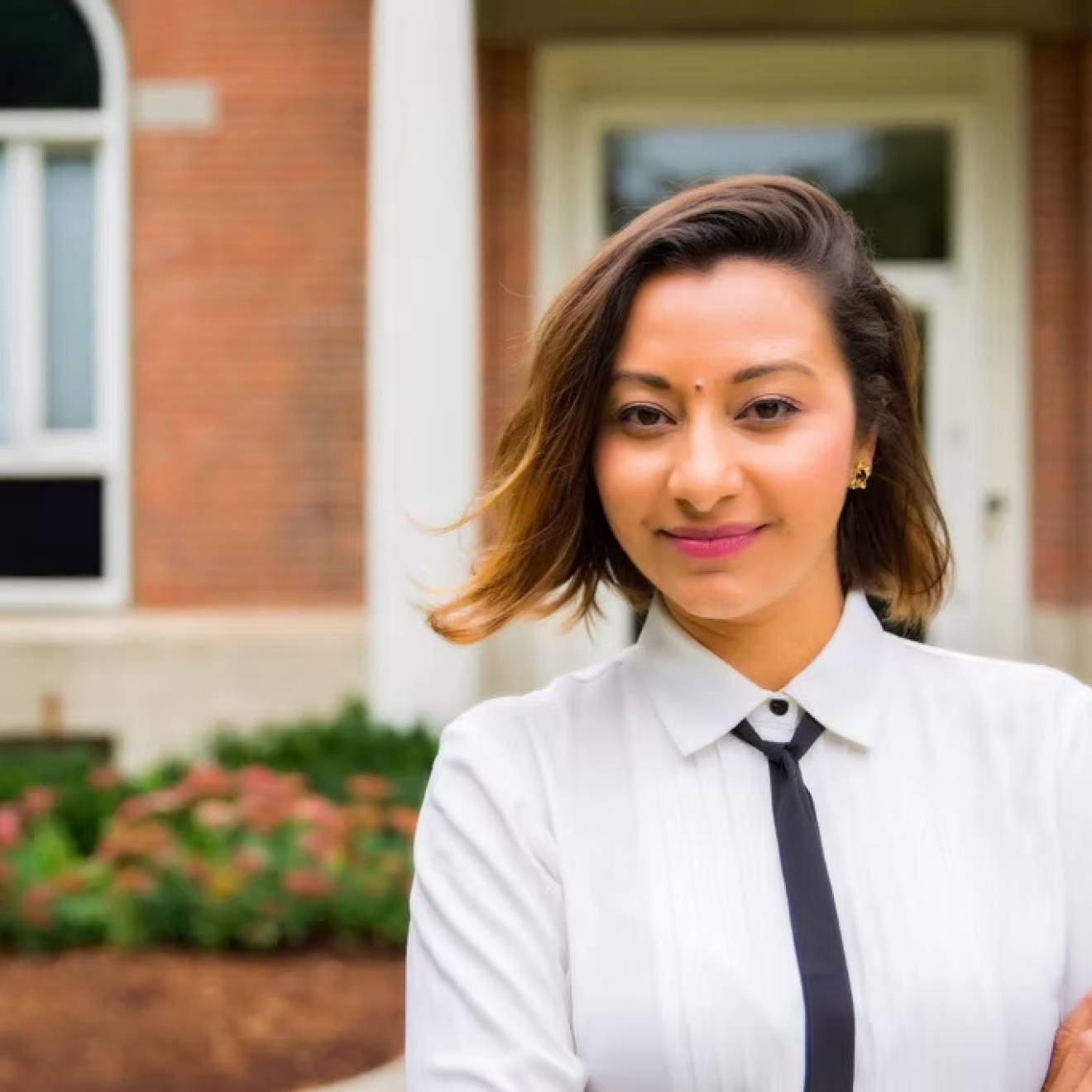 Study on Mexican American families A woman with a skinny tie and arms crossed smiles at camera