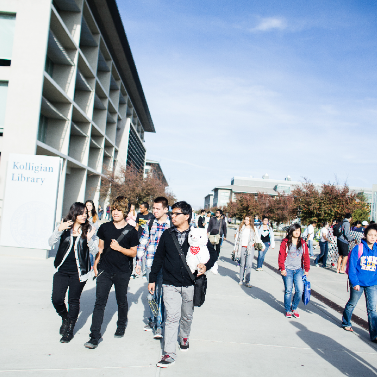 A group of students walking along the UC Merced campus, blue sky in background