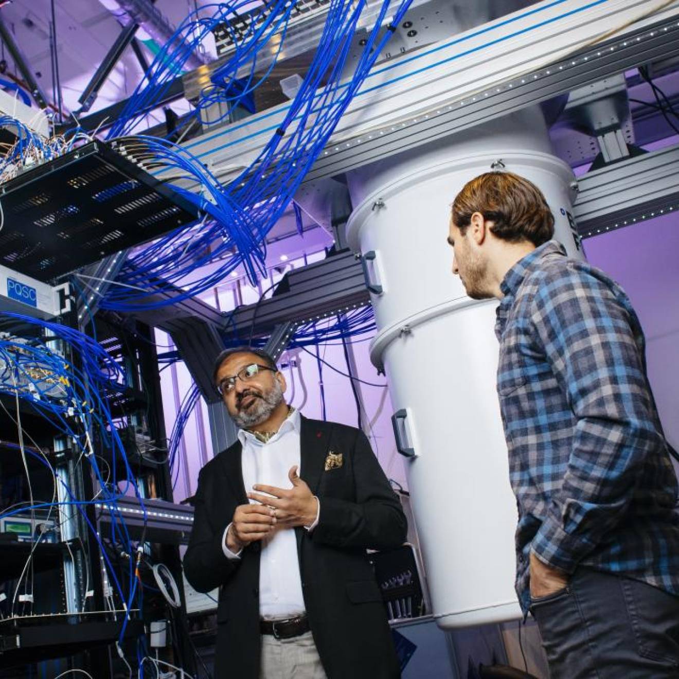 Three men talking in a quantum computing lab with purple lighting