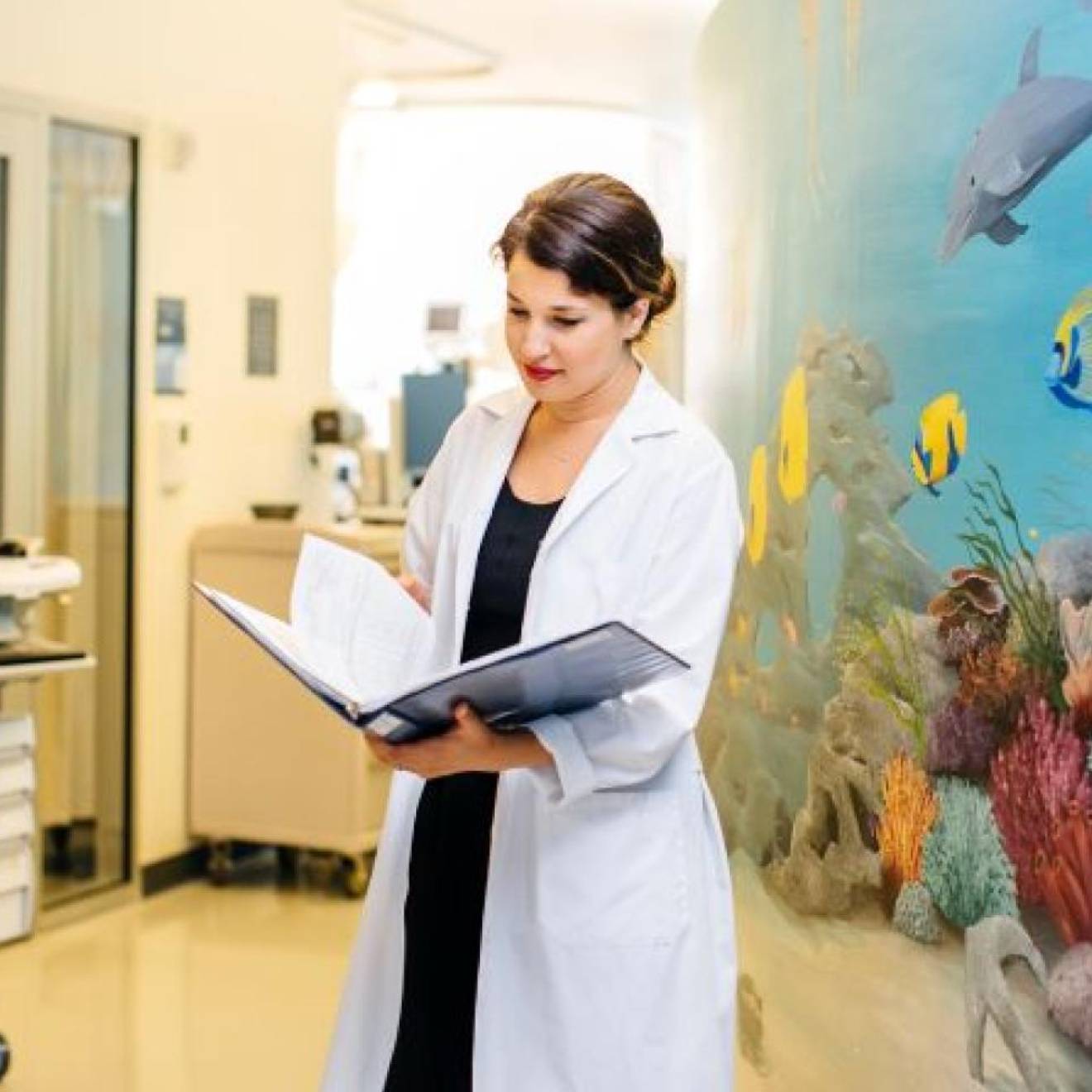 Woman doctor in white coat looks at a medical record with a colorful wall with an undersea mural behind her