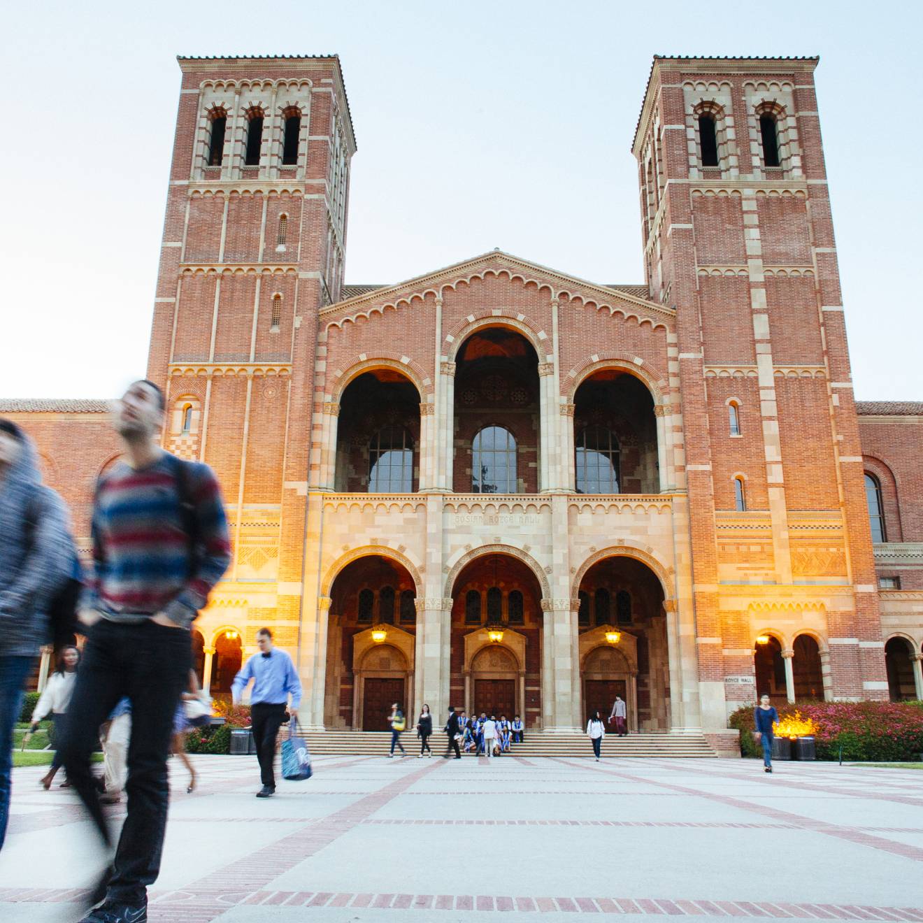 UCLA campus Students walk in front of a large building with two towers, Royce Hall, on the UC campus as evening begins to fall