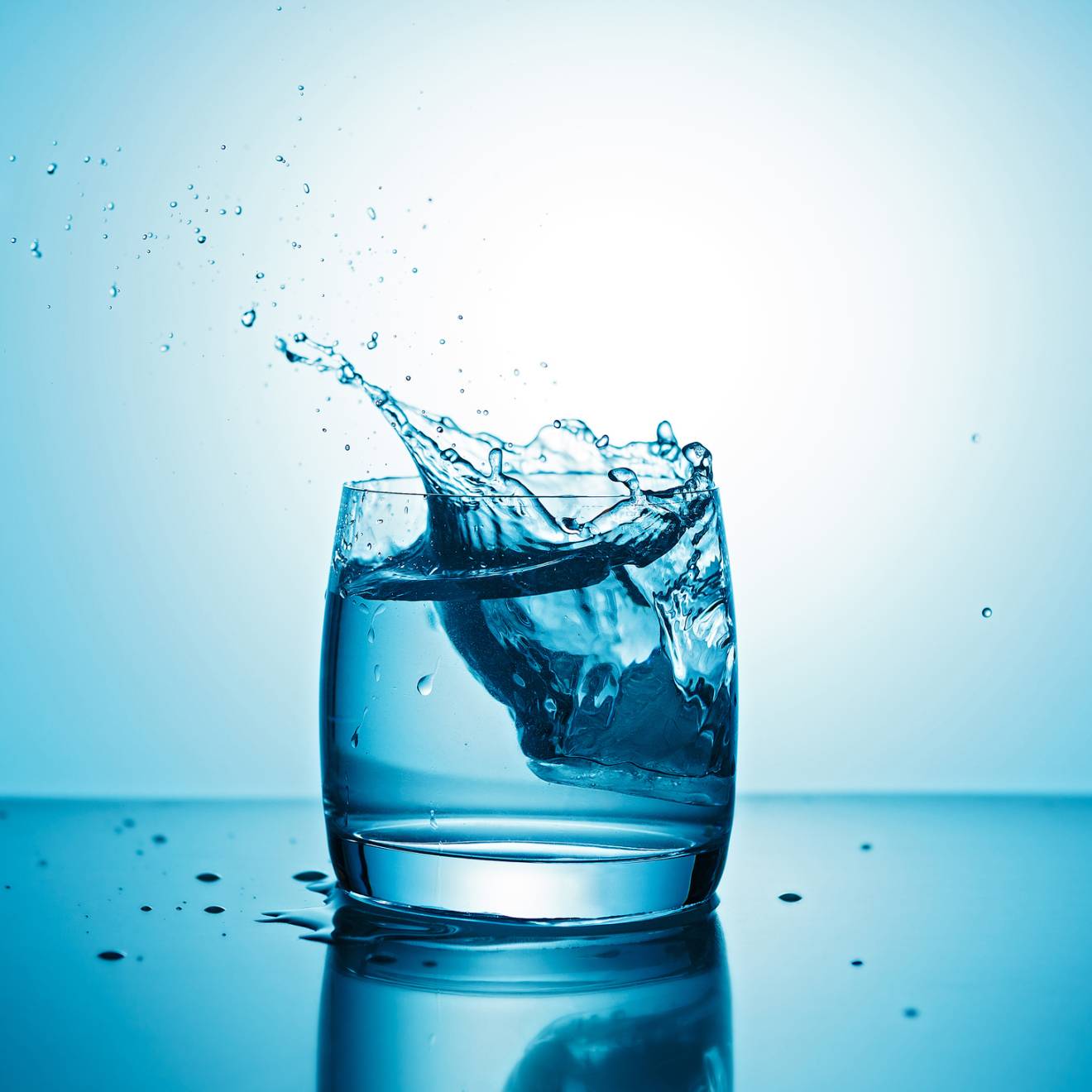 A glass of water with some water splashing out on a blue background