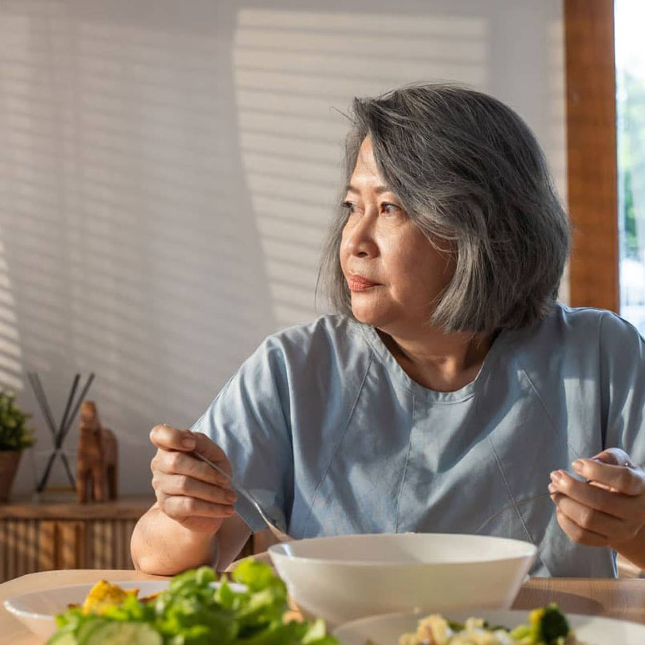 Older Asian woman eating alone, looking wistful