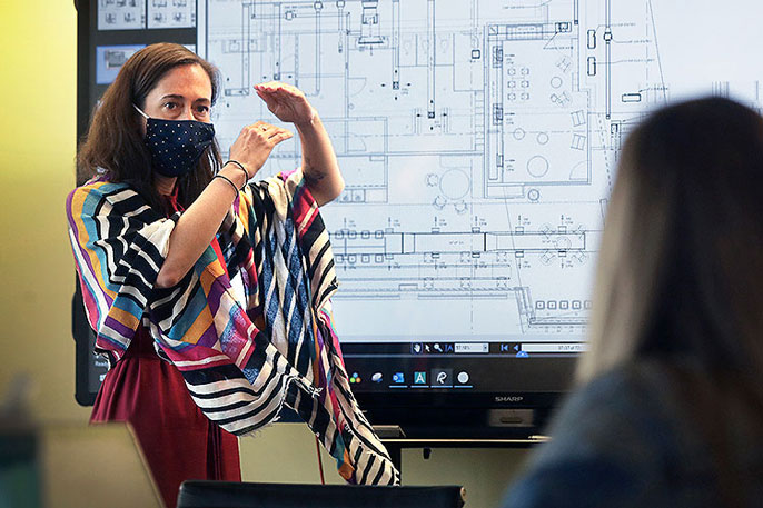 Woman explaining something in front of a large screen with architectural plans to a colleague